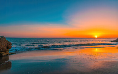 Obraz premium Vibrant sunset over the ocean with colorful sky and gentle waves on the beach
