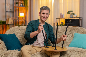 Young man at home repairs small wooden table with calm focus, appearing satisfied with progress and effort. Caucasian guy on sofa looks concentrated while enjoying handywork and fixing furniture part