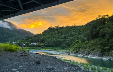 August dawn in Wulai, New Taipei City, Taiwan: orange sky, forested hills, river, and rural homes.