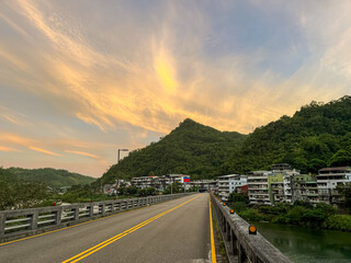 Empty bridge road leading into the village houses in Wulai, New Taipei City, Taiwan, set against a stunning golden and orange sunrise sky over lush green mountains.