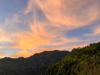 Spectacular sunrise sky with wispy pink and orange clouds above the dense, dark green mountain range in Wulai, New Taipei City, Taiwan, highlighting natural beauty.