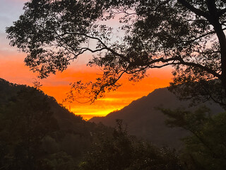 Striking orange and yellow sunrise illuminates the sky above a dark mountain valley silhouette in Wulai, New Taipei City, Taiwan, creating a dramatic and powerful scene.