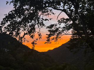Striking orange and yellow sunrise illuminates the sky above a dark mountain valley silhouette in Wulai, New Taipei City, Taiwan, creating a dramatic and powerful scene.