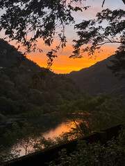 Golden sunrise light reflecting on Nanshi River, framed by overhanging tree branches and misty forested mountains in Wulai, New Taipei City, Taiwan.