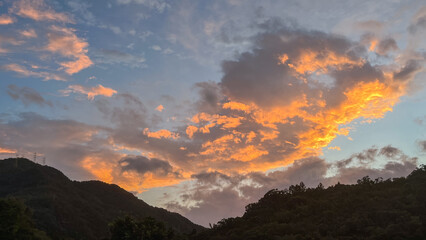 Vibrant sunrise or sunset sky over the lush green forest and distant mountains in Wulai New Taipei City Taiwan. Dramatic clouds in orange pink and blue hues.