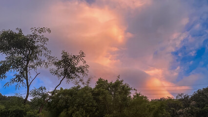 Soft pastel dawn sky with radiant orange and pink glowing clouds above lush treetops in Wulai, New Taipei City, Taiwan.