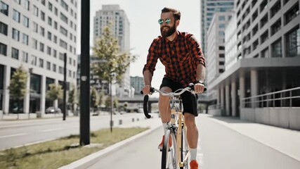 Young Man with Beard and Sunglasses Riding Bicycle in Urban Environment.