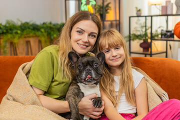 Lovely mother, daughter with french bulldog at home sit neat align to camera smile for family portrait. Woman and girl with dog on sofa hold pose show bond calm mood look happy photo memory together
