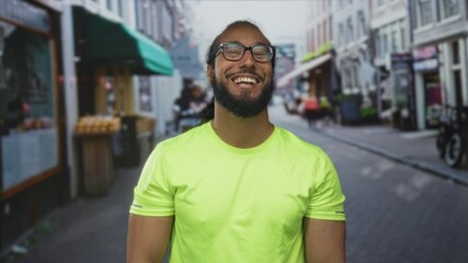 Man points finger toward camera on busy city street smiling broadly wearing neon green tshirt and glasses; joy connection candid moment.