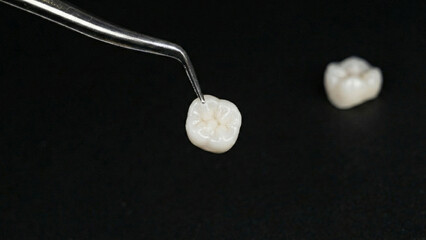 Macro close-up of a ceramic dental crown held by tweezers, isolated on black background with...
