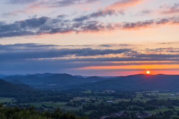 Sun setting behind rolling mountains in green valley