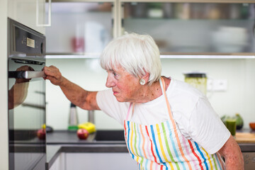 Senior woman cooking in the kitchen - eating and cooking healthy for her family; putting some potates in the oven, enjoying active retirement (shallow DOF; color toned image)