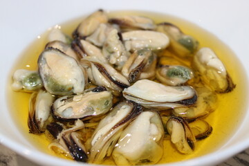 Fresh oysters in olive oil served on a white plate with a light background