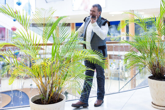 Emotional businessman recording voice messages on smartphone in modern office with green plants. High quality photo