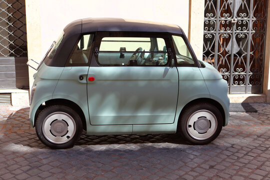 Side view of a vintage-inspired Fiat Topolino electric microcar parked on a cobblestone street in Rome, Italy. Modern Italian urban transportation.