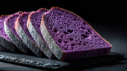 Sliced homemade purple bread made from ube sweet potatoe. Moody dark background.
