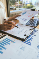 A person reviews financial charts while using a calculator and laptop on a desk, focusing on data analysis and business planning.