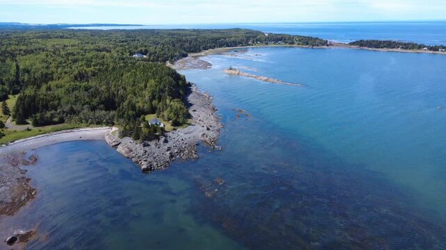 Spectacular aerial view of the rocky coast and lush vegetation of Pointe Mitis and its legendary lighthouse, perched at the tip of the point facing the St. Lawrence River, Metis-sur-mer, Quebec.