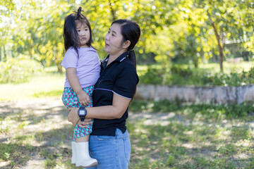 Fototapeta premium Happy mother with her daughter spending time together in park,A beautiful young mother is holding her cute little Asian daughter in a park during her vacation.