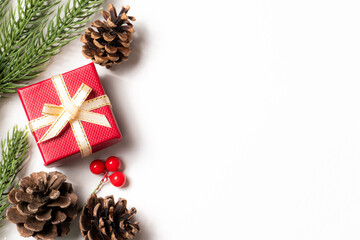 Flat lay Christmas composition with red gift box, pinecones, fir branches, and berries on white background. Ideal for holiday greeting cards, seasonal banners, and winter promotional designs.