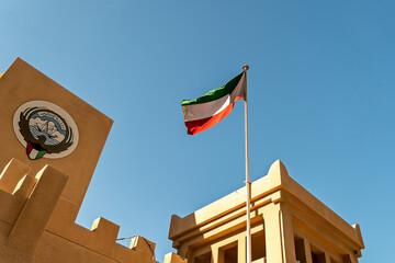 Kuwaiti national flag and state emblem on a traditional government building under clear blue sky. Symbol of national pride, culture, and heritage in Kuwait City.