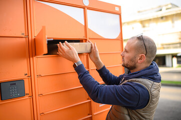 Fototapeta premium Man collecting multiple parcels from a self-service parcel locker, using digital code on the screen. Modern urban delivery, contactless pickup and fast online shopping concept. 