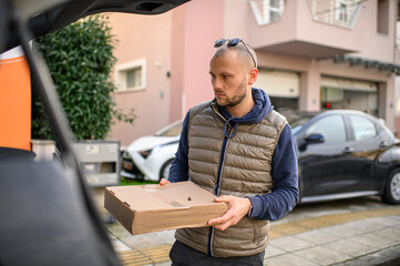 Man loading a parcel into the trunk of his car, preparing for delivery or transport. Modern logistics, online shopping and everyday courier tasks concept.