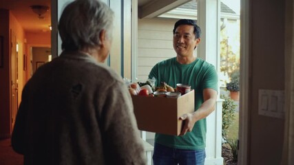 Asian man delivering a box of groceries to a senior woman at her front door. Volunteer providing food assistance to an elderly lady. Charity and community support concept