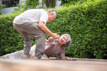 Senior woman falling on ground and receiving help from caregiver, Elderly accident outdoors with man assisting injured senior woman, Senior emergency situation with older man helping fallen woman