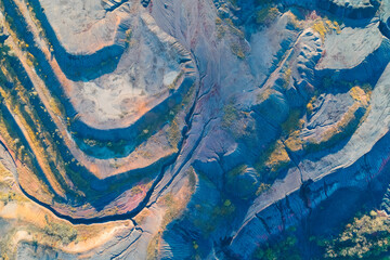 Drone perspective of a colossal quarry. The sweeping curved layers and vibrant blue and orange hues create a geological abstract pattern, symbolizing environmental destruction from extraction