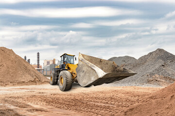 A loader works at a construction site, moving sand and gravel among large mounds. Industrial...