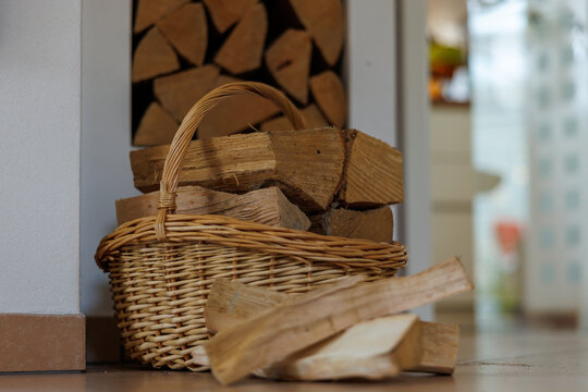A cozy indoor scene featuring a wicker basket filled with neatly cut firewood placed beside a stack of logs.