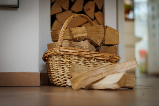 A cozy indoor scene featuring a wicker basket filled with neatly cut firewood placed beside a stack of logs.