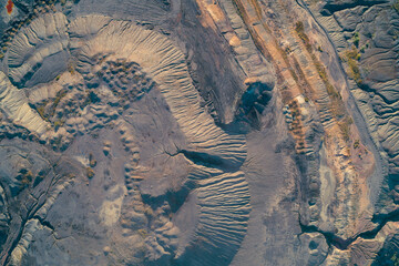 Top-down drone shot showing intricate patterns of eroded land, deep gullies, and dark industrial waste. The severe environmental devastation and geological disruption caused by mining
