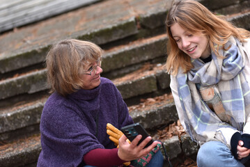 Mother and young adult daughter sitting on steps using a smartphone in a park