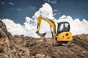 Obraz premium Excavator performs earthmoving tasks at a construction site, surrounded by dirt and rocks with a bright blue sky and puffy clouds above