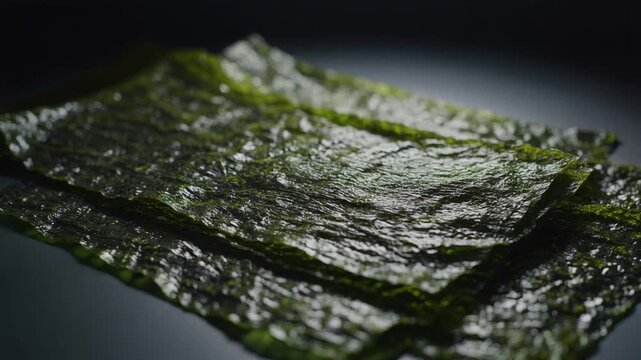 Stack of textured, dark green nori sheets on a dark surface, with soft lighting