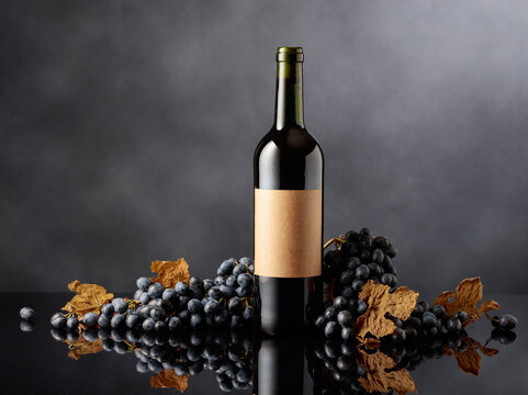 Bottle of red wine with blue grapes on a black reflective background. - Powered by Adobe