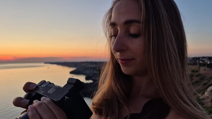 Woman photographer camera, young female adjusting settings on professional camera, capturing a beautiful sea sunset landscape
