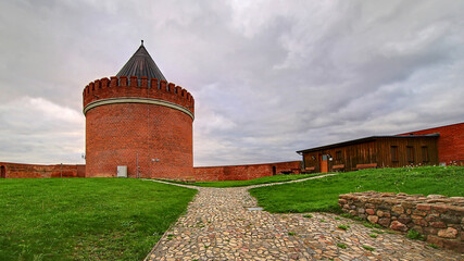 Round brick tower of castle Lindau with cobblestone path and surrounding fortress under gray clouds