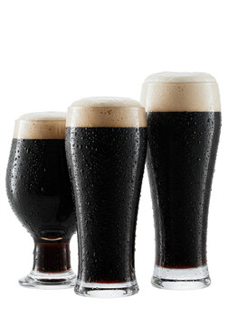 four different tall beer glasses filled with opaque black stout, shimmering condensation highlights extreme coldness on a transparent background. concept for beverage advertising