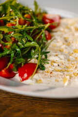 Close-up of arugula and cherry tomato salad with creamy dip drizzled with olive oil.