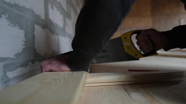 Close-up of a worker cutting a wood plank with a hand saw during floor installation. Real manual construction process.