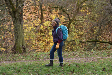 Woman hiking in a forest wearing a purple sweater and a blue backpack