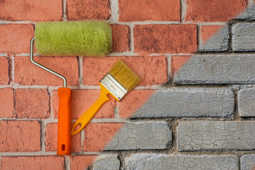 A creative background for renovation. A roller and brush are placed against a backdrop of red and gray brickwork. Renovation tools
