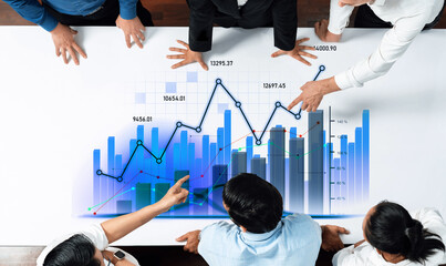 A group of business professionals collaborates around a table, analyzing financial data and interactive charts, highlighting teamwork and strategic insights. Scalp