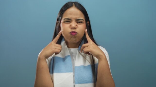 Young woman with blue scarf making funny faces over isolated blue background, showcasing playful expressions and emotions.
