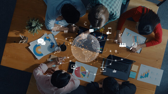 A diverse team collaborates around a table with charts and technology, analyzing data and discussing strategies for informed decision-making and growth. Trope