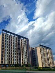 Contemporary apartment blocks surrounded by greenery, standing tall under beautiful blue skies and striking cloud patterns.