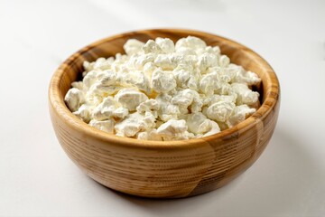 A wooden bowl filled to the brim with fresh white cottage cheese on a white surface in bright light